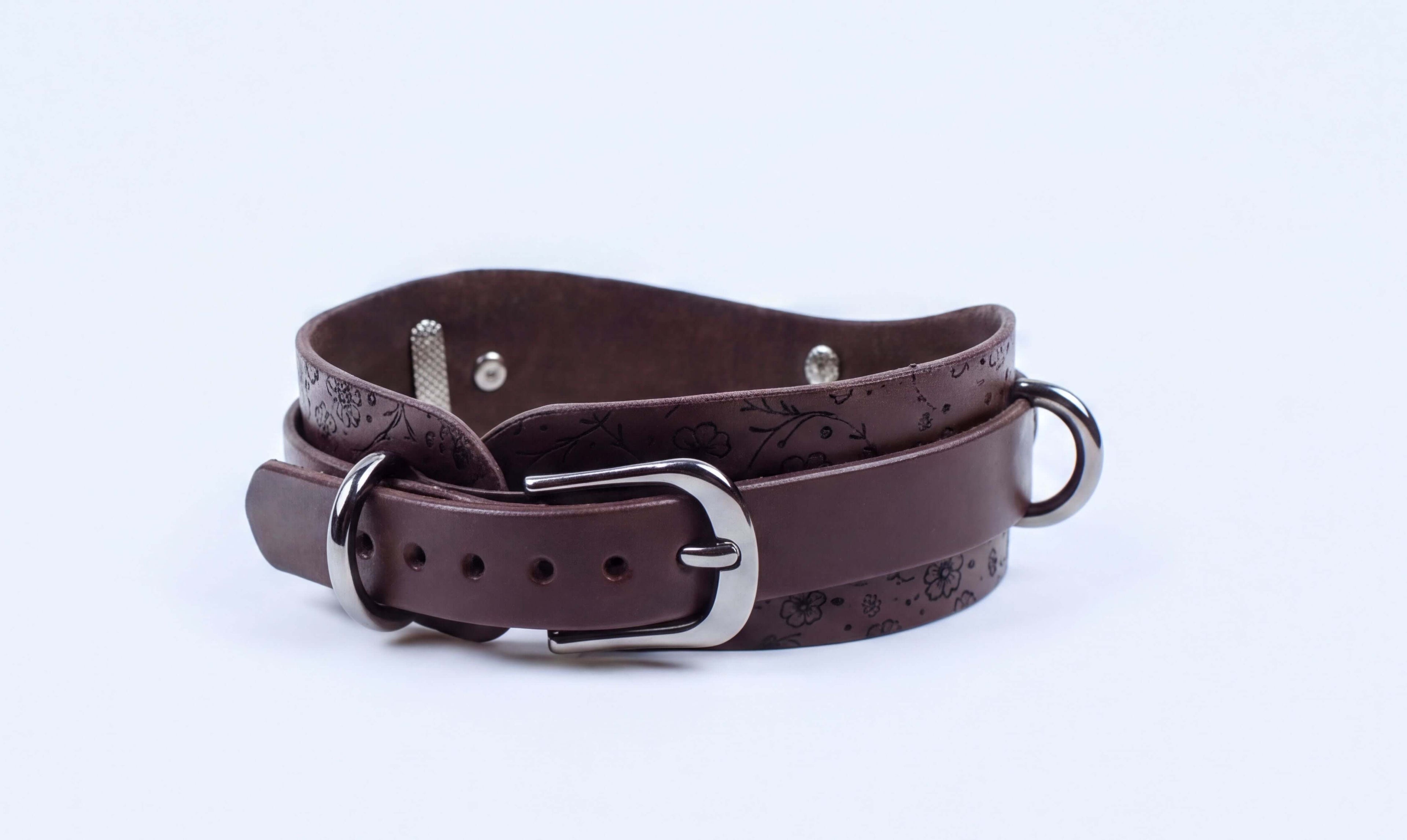 A brown leather dog collar with a metal buckle and a decorative pattern on the leather.