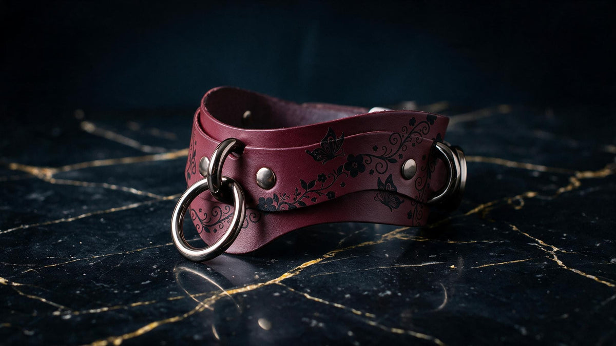 A burgundy leather choker necklace with metal rings and a floral pattern is displayed on a dark marble surface.