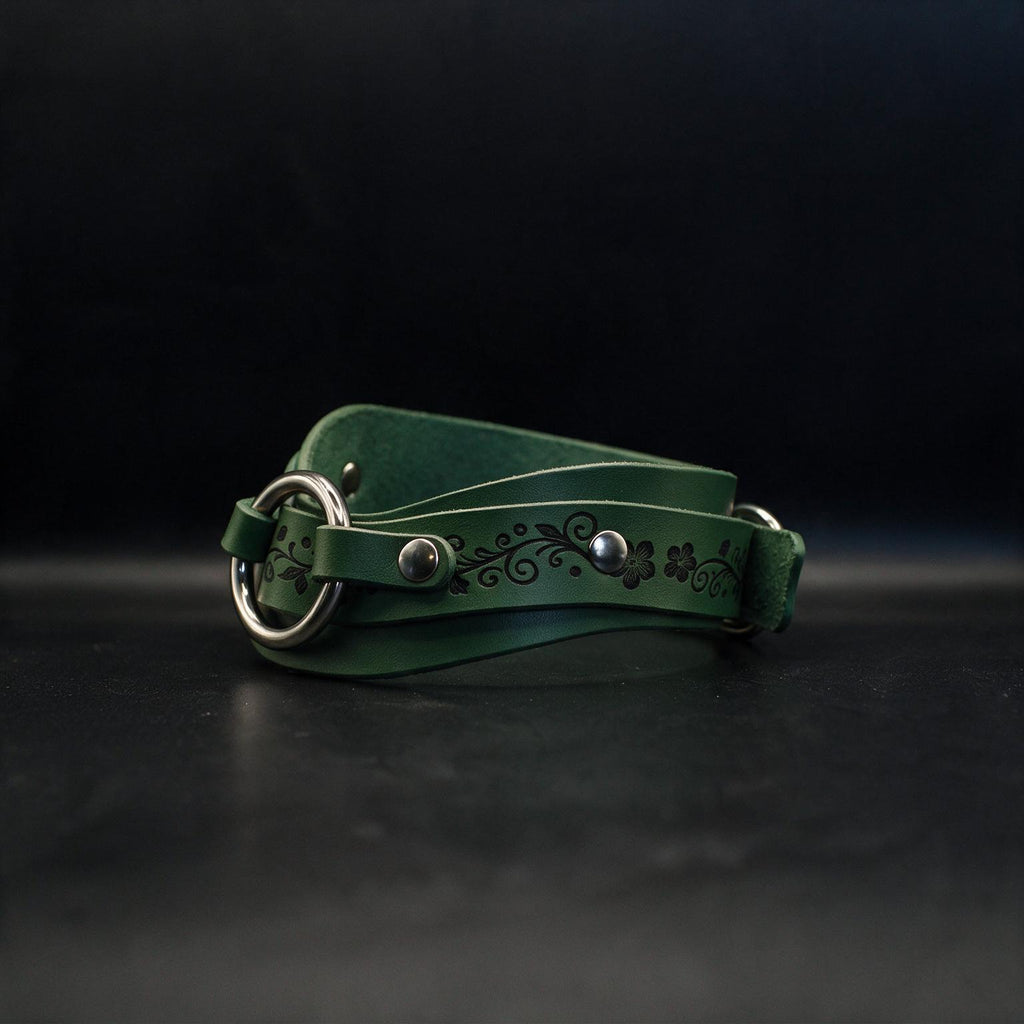 A green leather belt with a metal buckle and floral design on the strap is shown against a dark background.