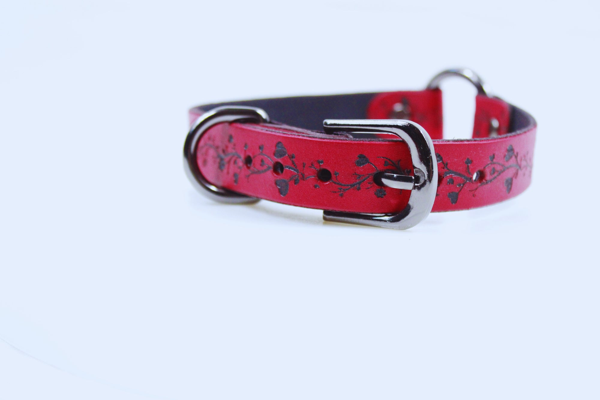 A red leather dog collar with a floral pattern and metal buckle.