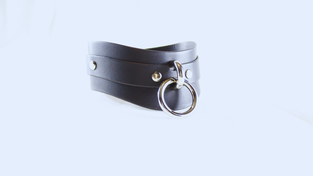A black leather choker necklace with a metal ring and two metal studs on the front.