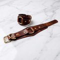 a brown leather strap with gold-colored buckles and a gold-colored buckle, resting on a marble surface.