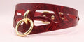 A close-up image of a burgundy leather choker necklace with a gold-colored ring and a cutout design on the front.