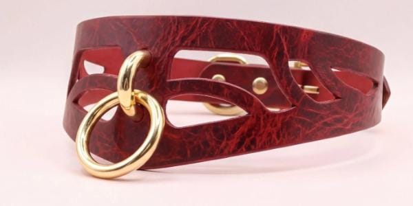 A close-up image of a burgundy leather choker necklace with a gold-colored ring and a cutout design on the front.