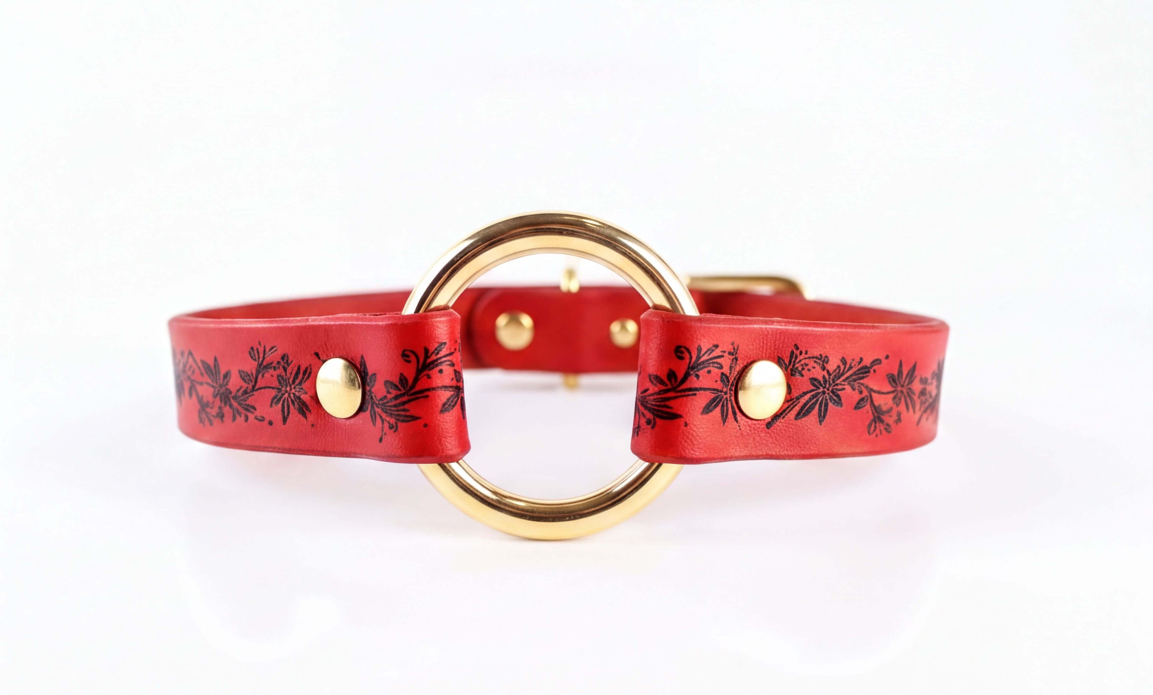 A red leather strap with a gold-colored circular buckle, featuring black floral designs.