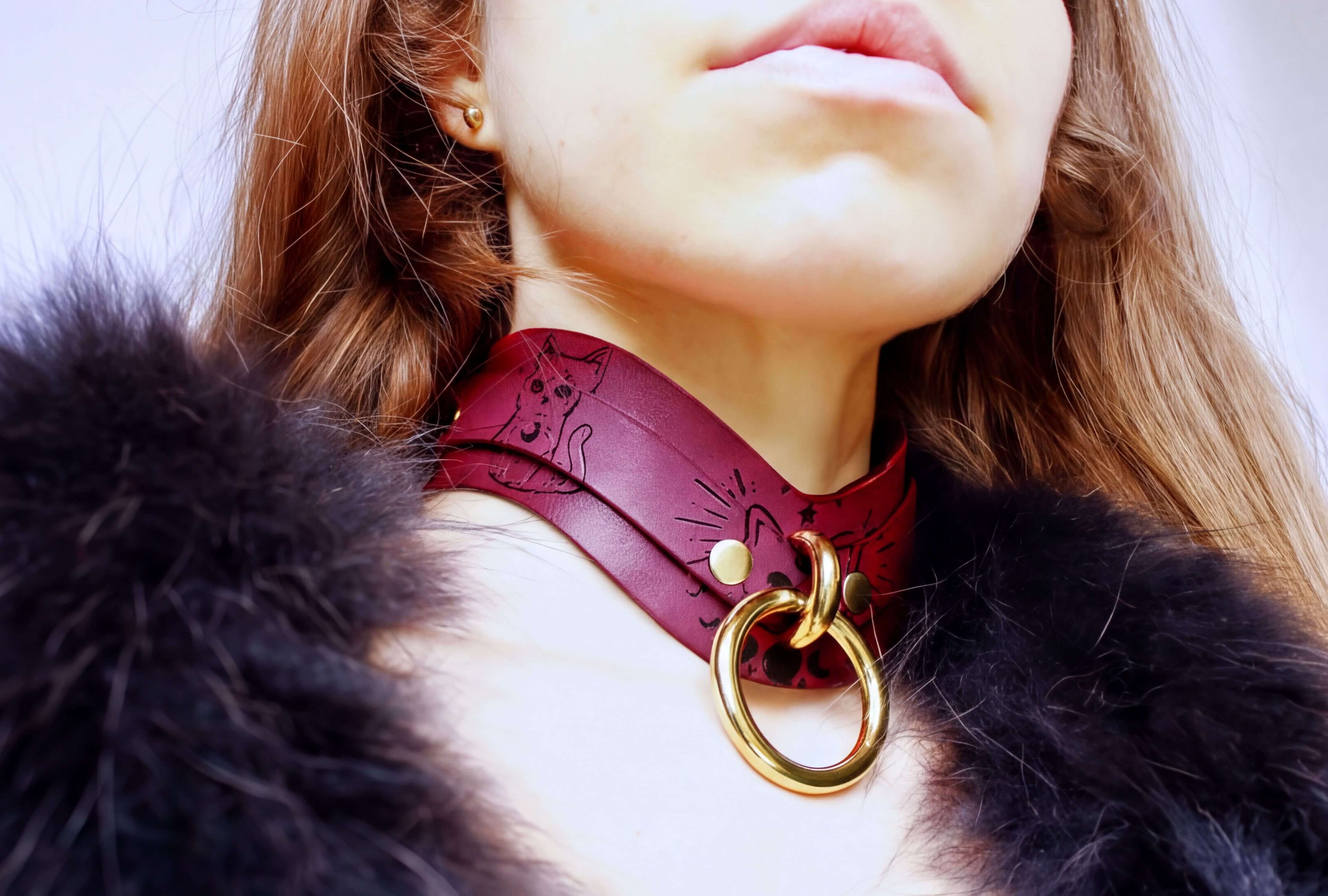 A close-up of a person wearing a burgundy choker necklace with a cat design and a gold ring.