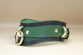 A green leather choker with a dark green floral pattern and two gold-colored metal rings on either side.