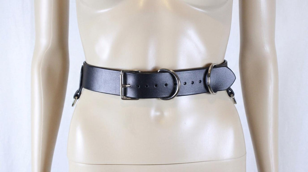 A mannequin wearing a black leather belt with metal rings and buckles.