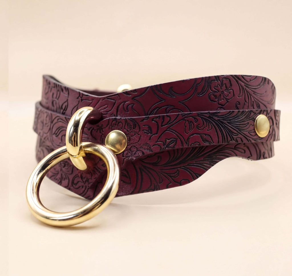 A burgundy leather choker necklace with a gold-colored ring and two gold-colored metal studs.