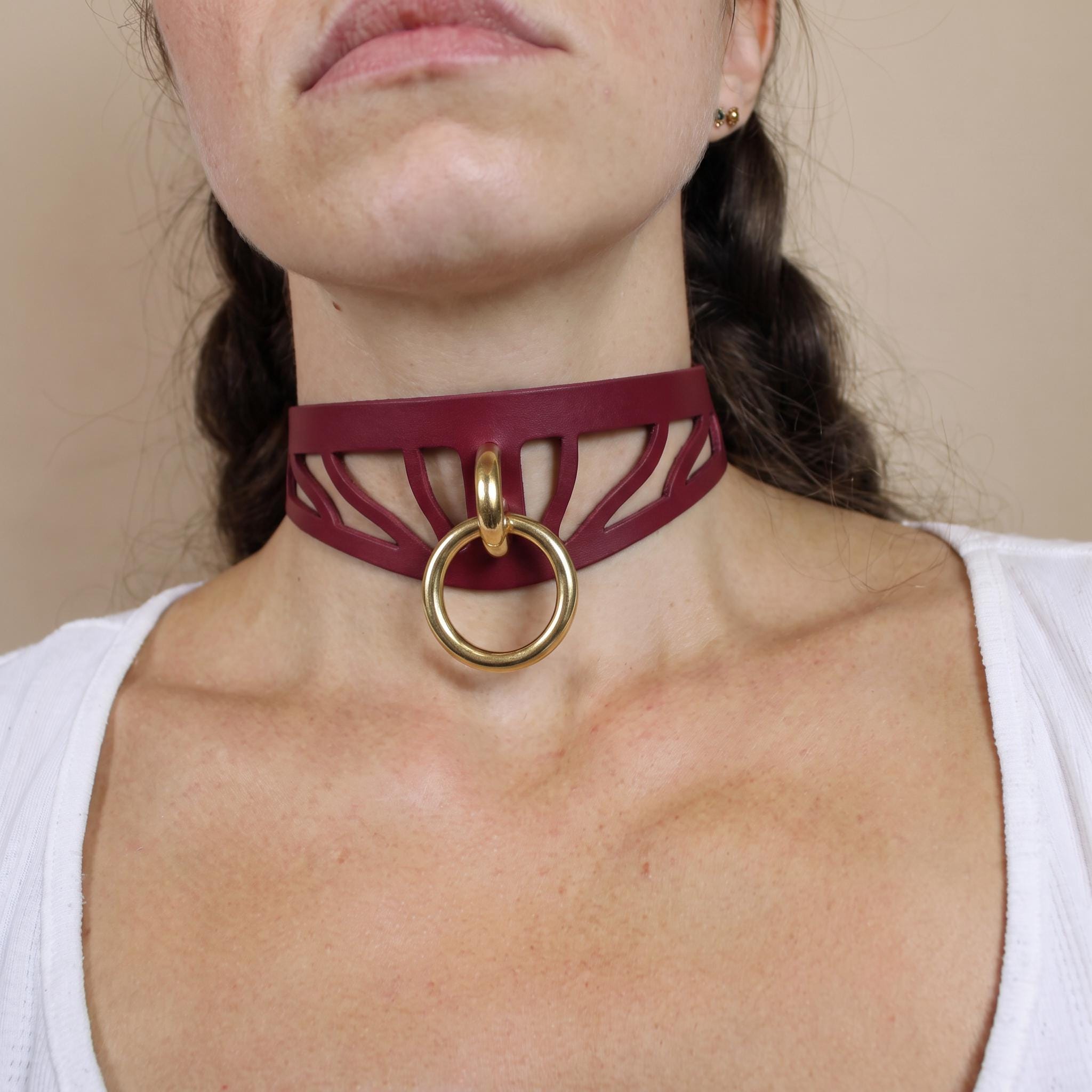 A close-up of a woman's neck and chest area wearing a burgundy choker necklace with a gold ring.