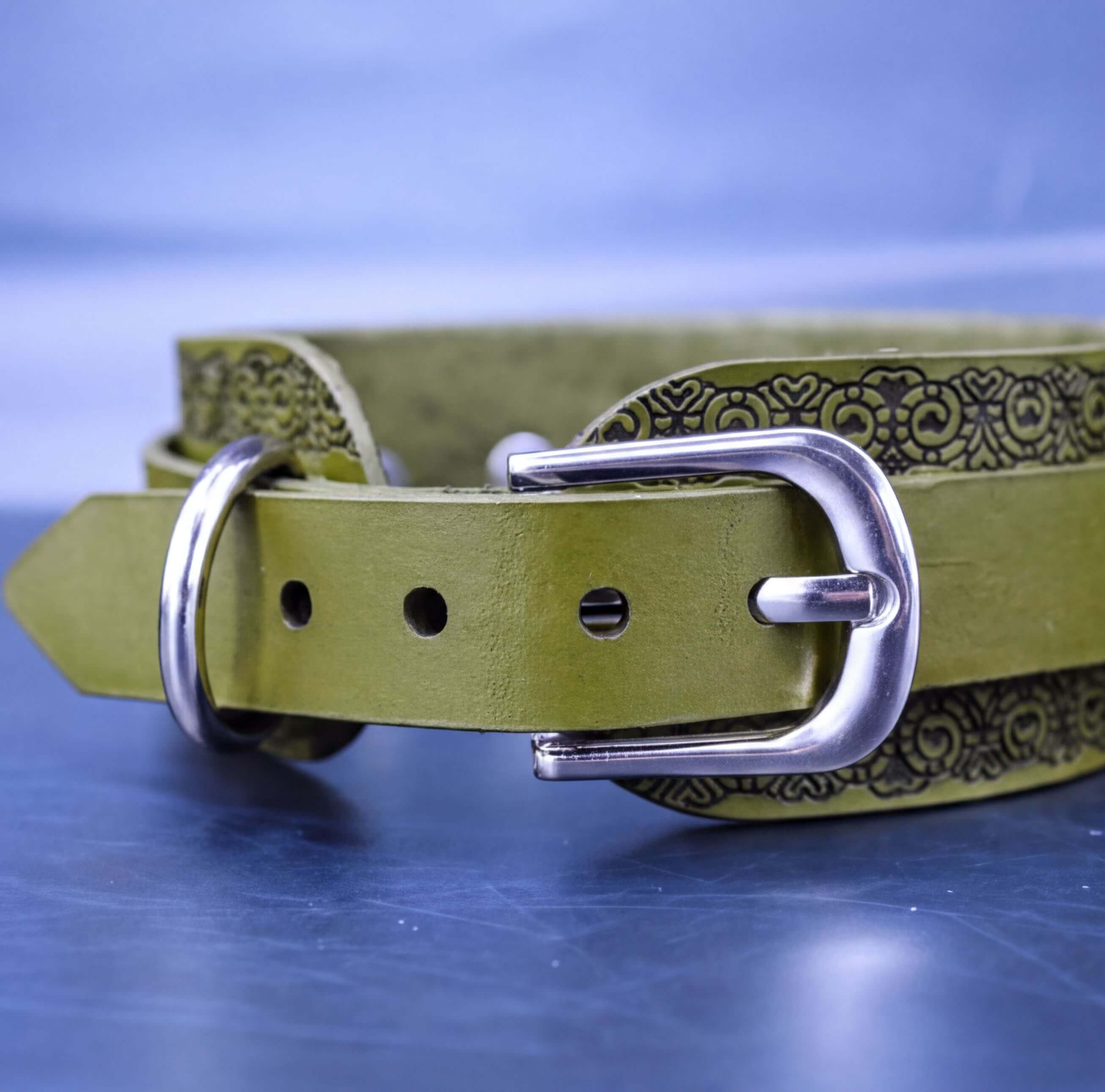 A close-up view of a green leather belt with a metal buckle, resting on a blue surface.