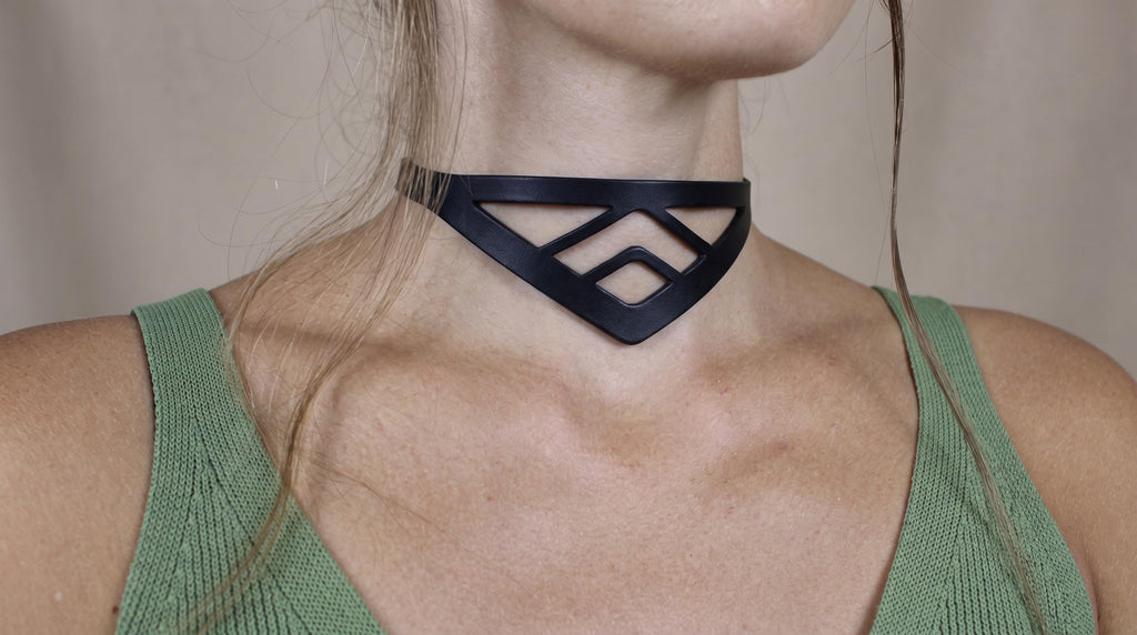 A close-up of a woman's neck and chest area wearing a black choker necklace with a geometric pattern.