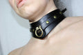 A close-up of a person's neck wearing a black leather choker with gold hardware.