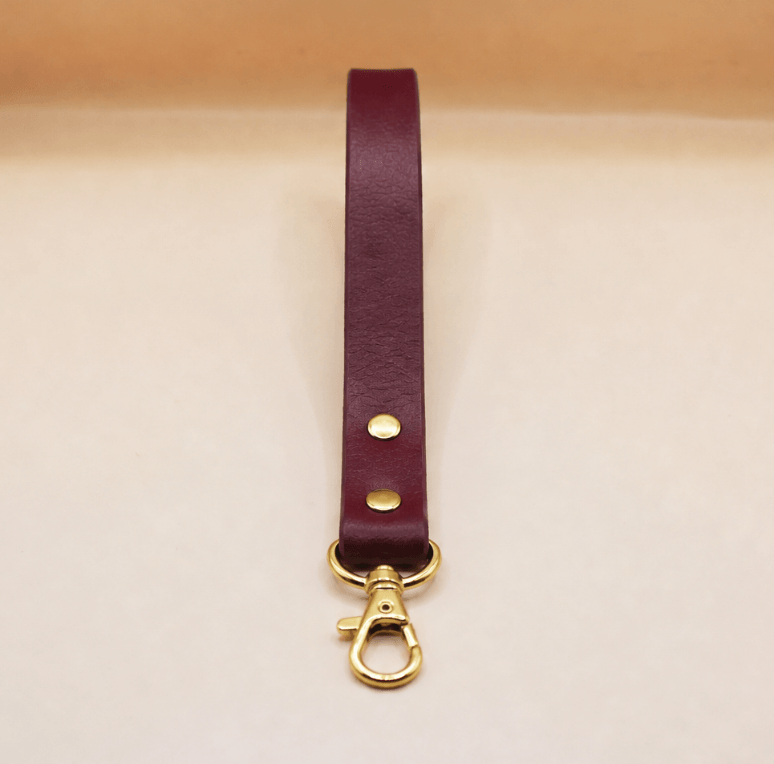 A burgundy leather strap with a gold-colored metal clasp and hook is shown against a light-colored background.
