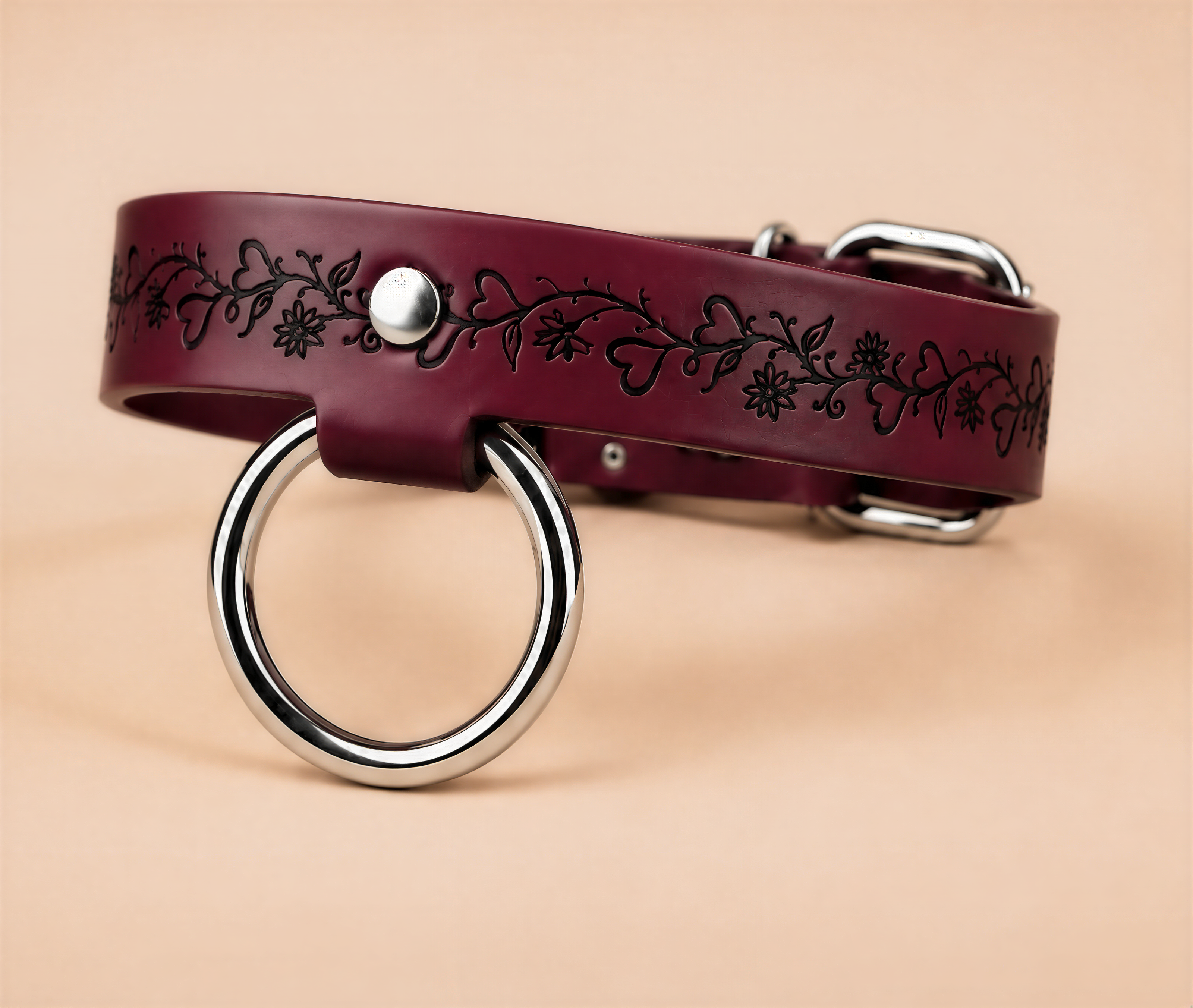 A burgundy leather collar with a metal ring and floral design on the strap.