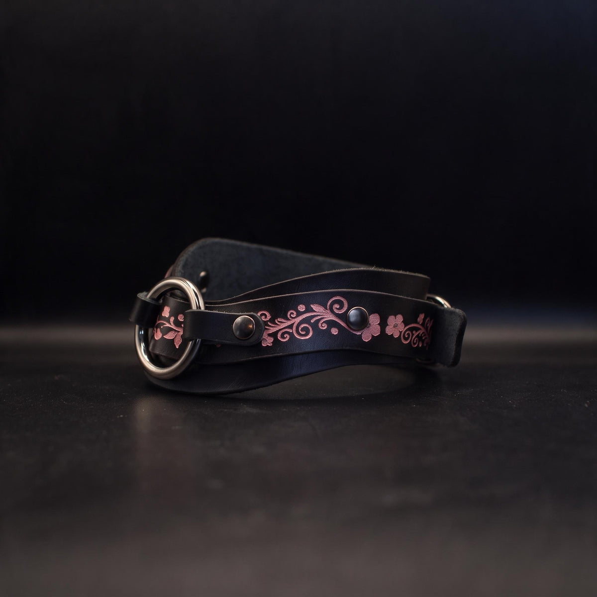 A black leather belt with a floral design on it, resting on a dark surface.