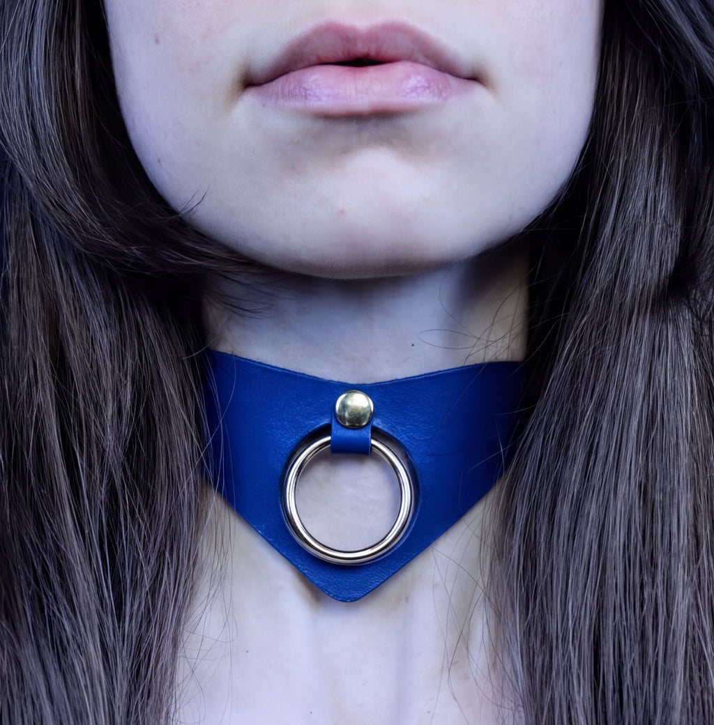 A close-up of a woman's neck and chin area, featuring a blue choker necklace with a metal ring.