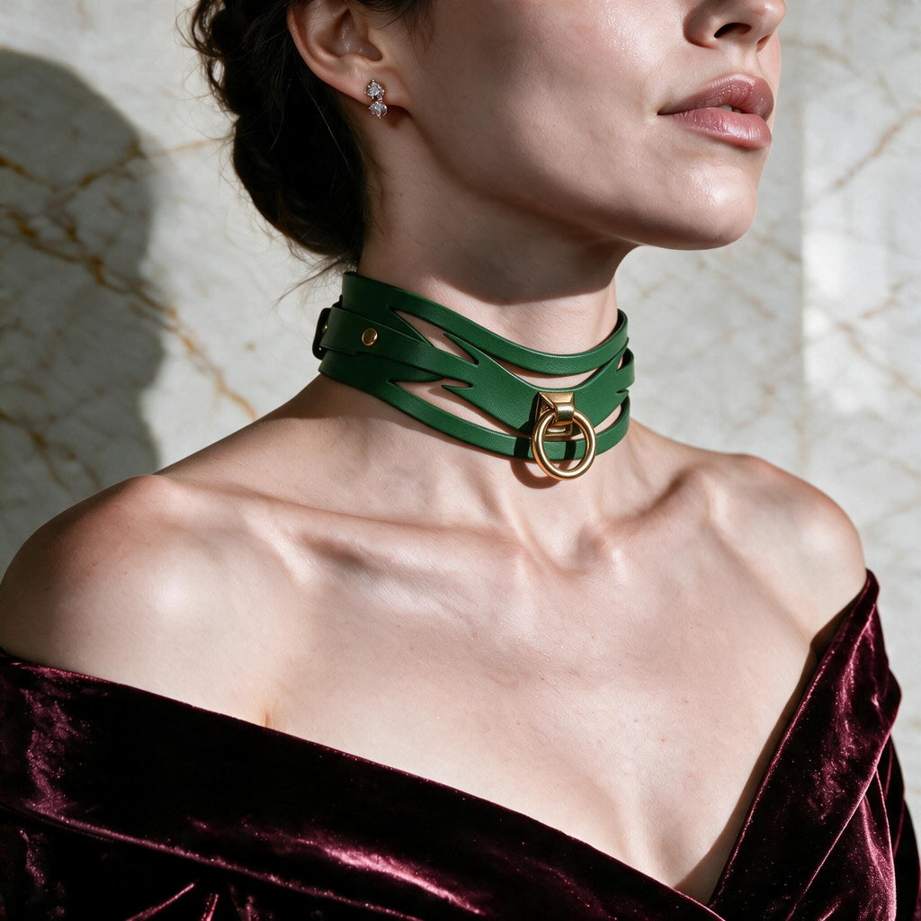 A woman wearing a green choker necklace with a gold ring, posing against a marble wall.