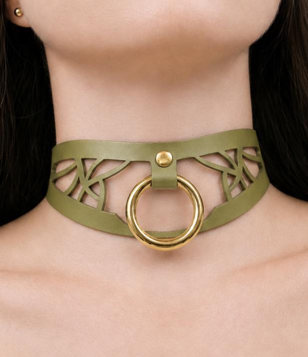 A close-up of a woman's neck wearing a green choker necklace with a gold ring.