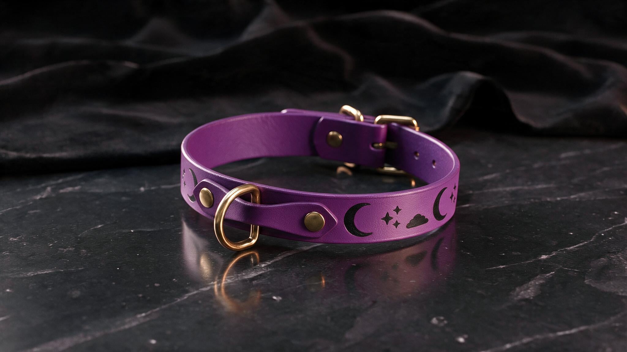 A purple leather collar with a crescent moon and star design on it, resting on a dark surface.