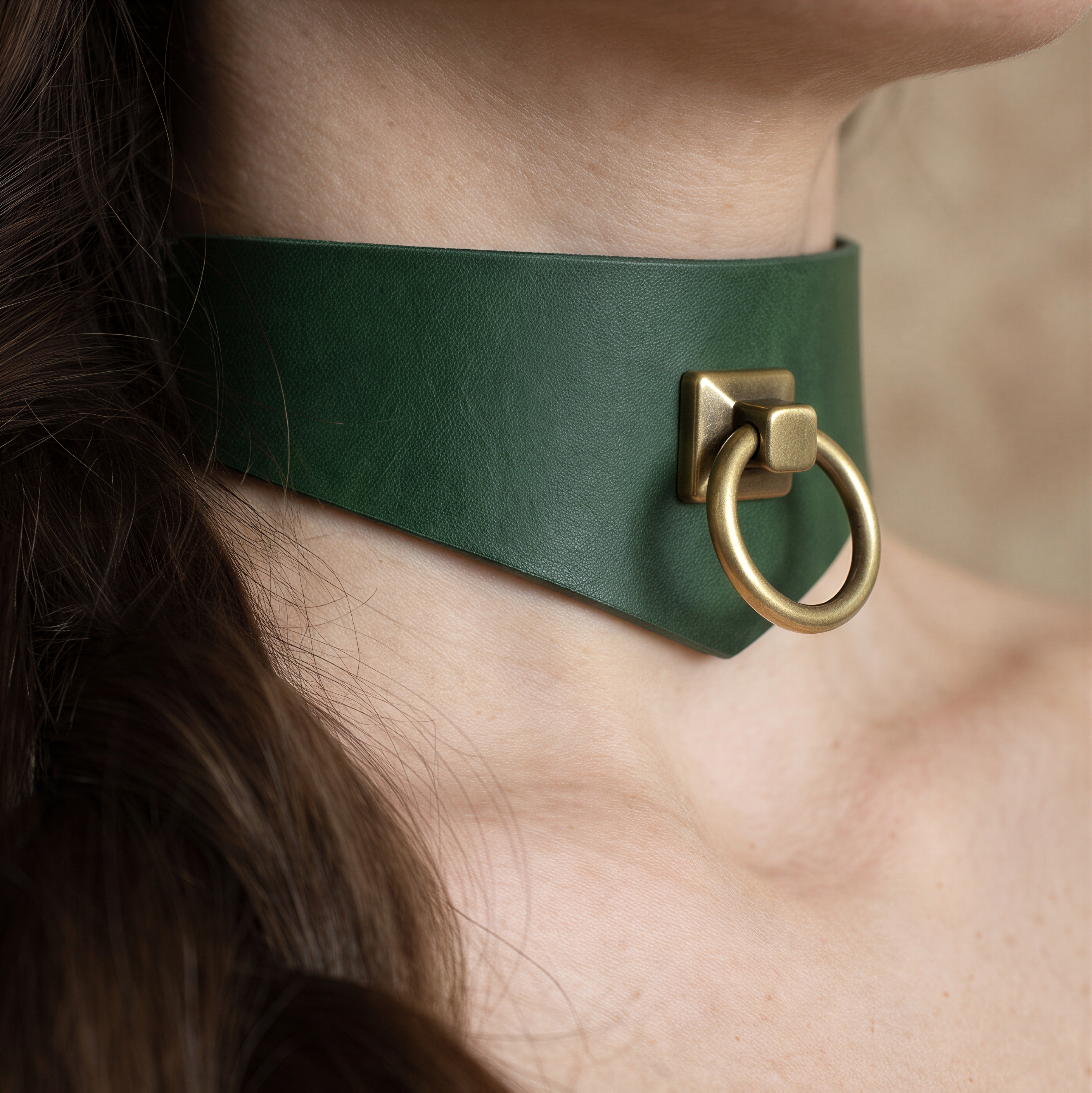 A close-up view of a woman's neck and chin area, featuring a green leather choker necklace with a brass-colored metal ring.