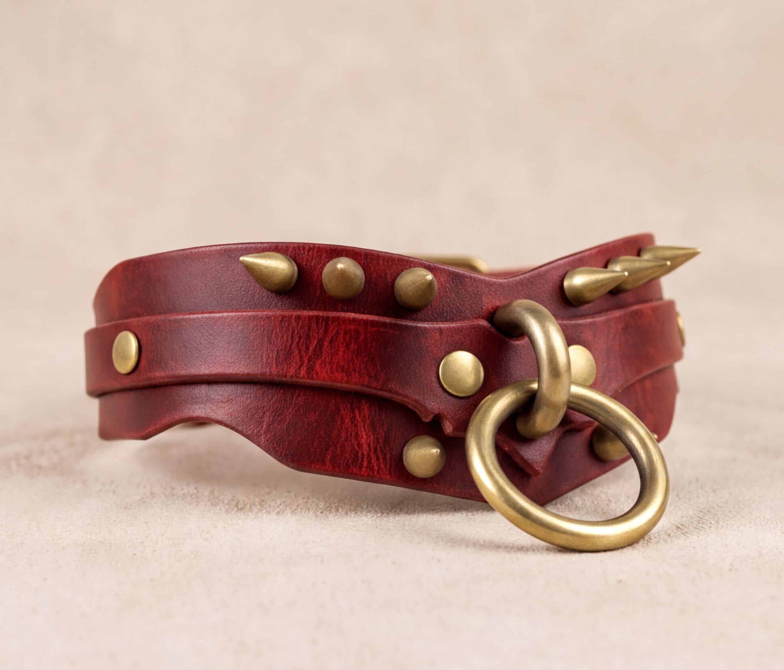 A red leather collar with metal studs and a metal ring attached to it.