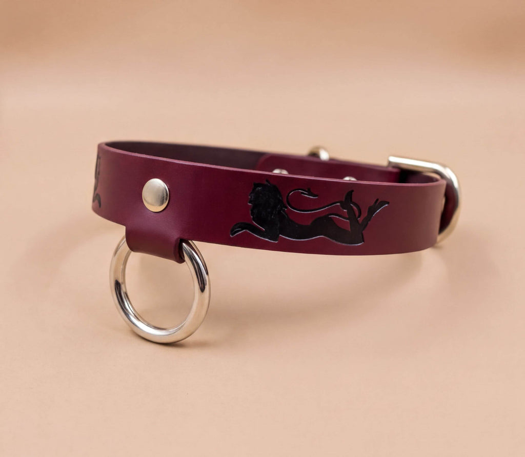 A burgundy leather dog collar with a black lion design and metal ring.