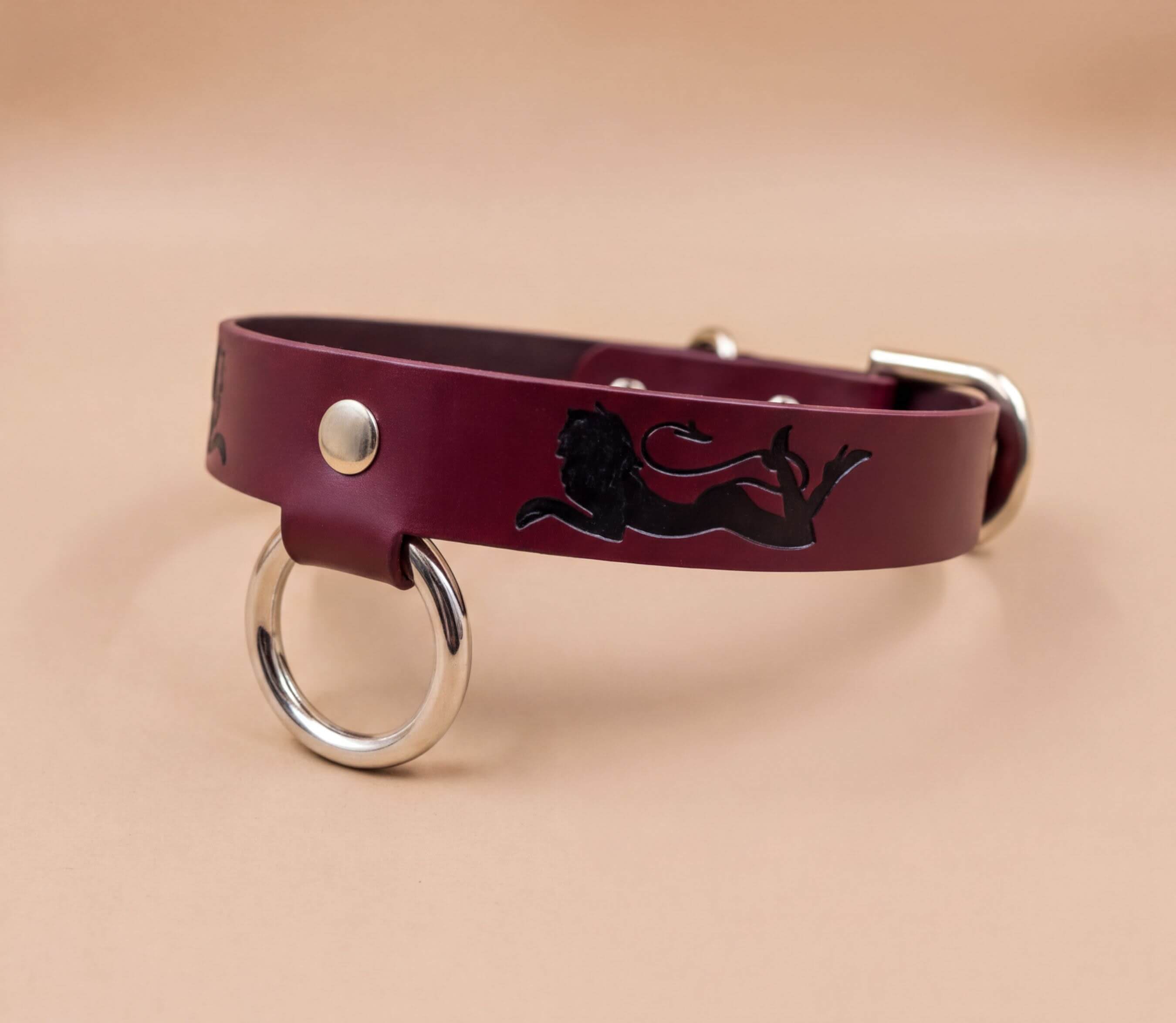 A burgundy leather dog collar with a black lion design and metal ring.