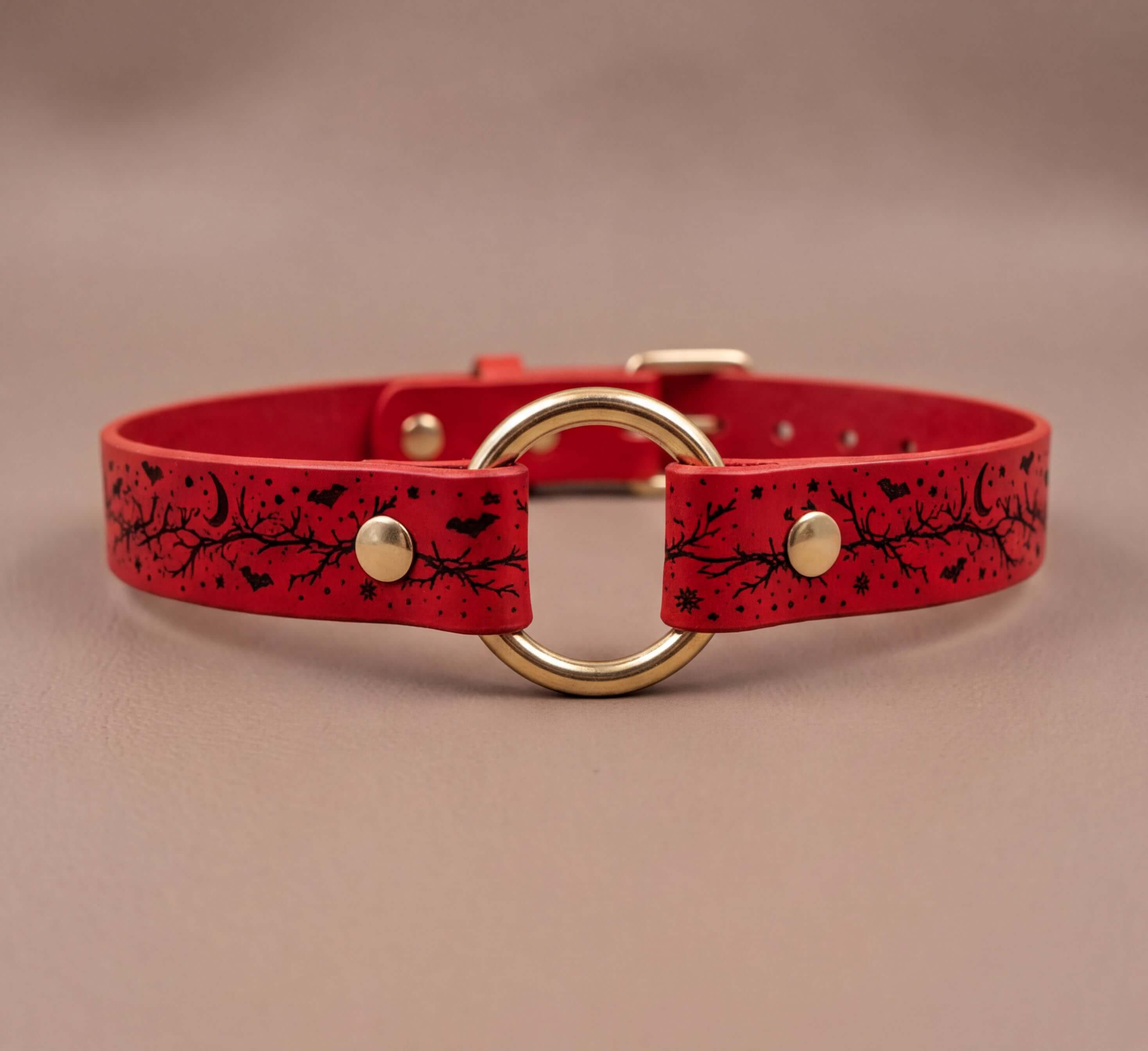 A red leather collar with a gold-colored circular buckle and a black design featuring bats and stars.