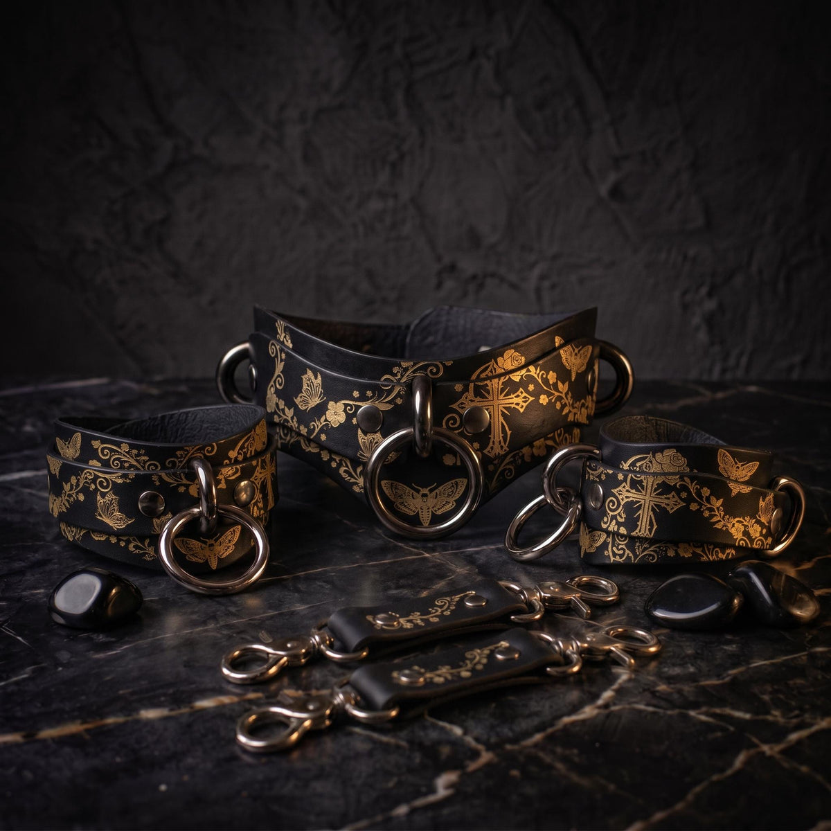 a collection of ornate leather straps and buckles, each adorned with intricate gold designs, displayed on a dark surface.