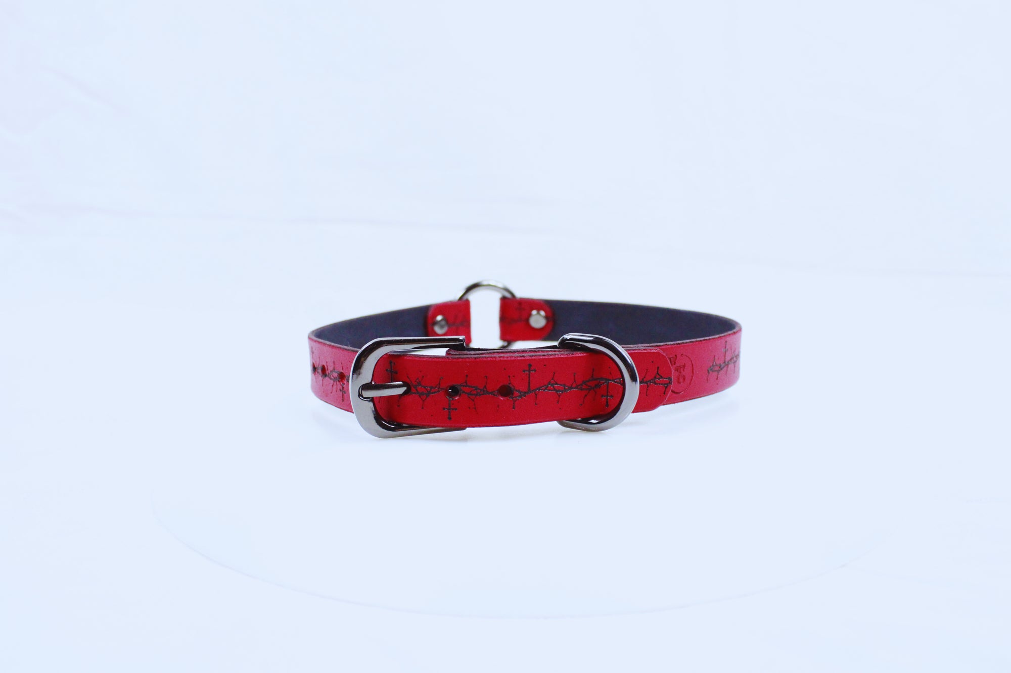 A red leather dog collar with a metal buckle and a decorative pattern on the strap.