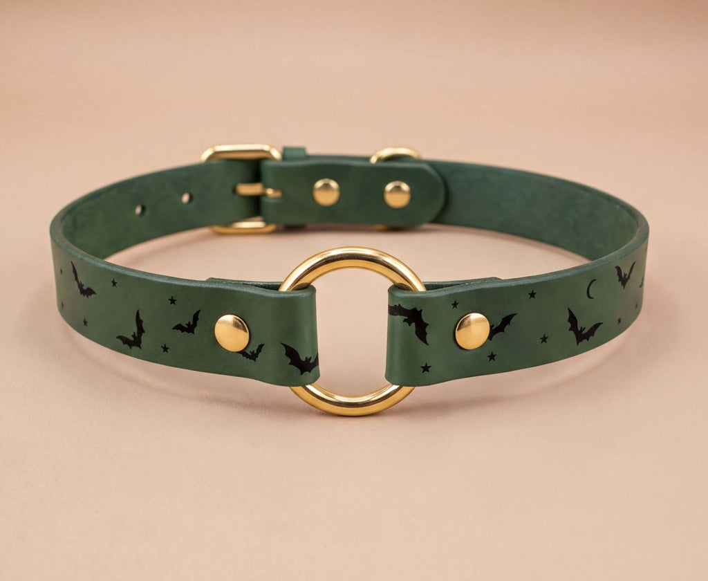 A green leather collar with a gold ring and bat designs printed on it.
