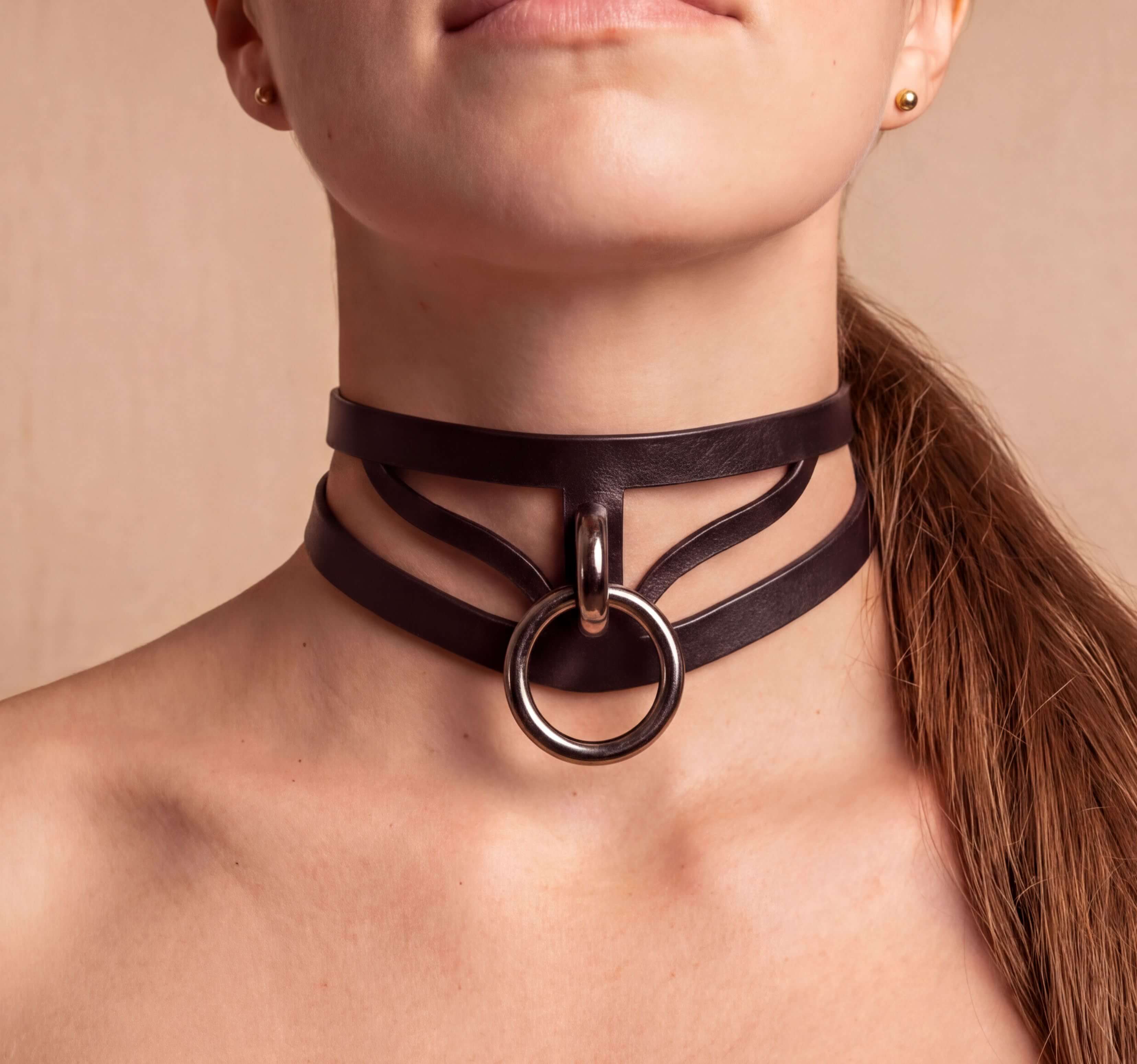 A close-up of a woman's neck and chest area wearing a black leather choker necklace with a large circular ring.