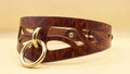 A brown leather choker necklace with a gold-colored metal ring and a cutout design.