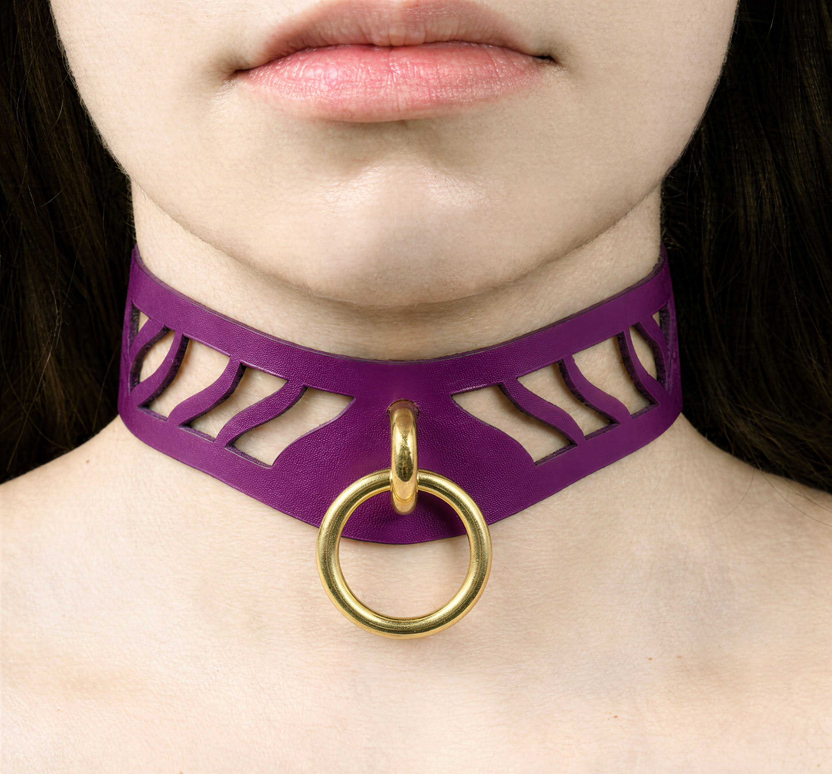 A close-up of a woman's neck and chin area, featuring a purple choker necklace with a gold ring and a cutout design.