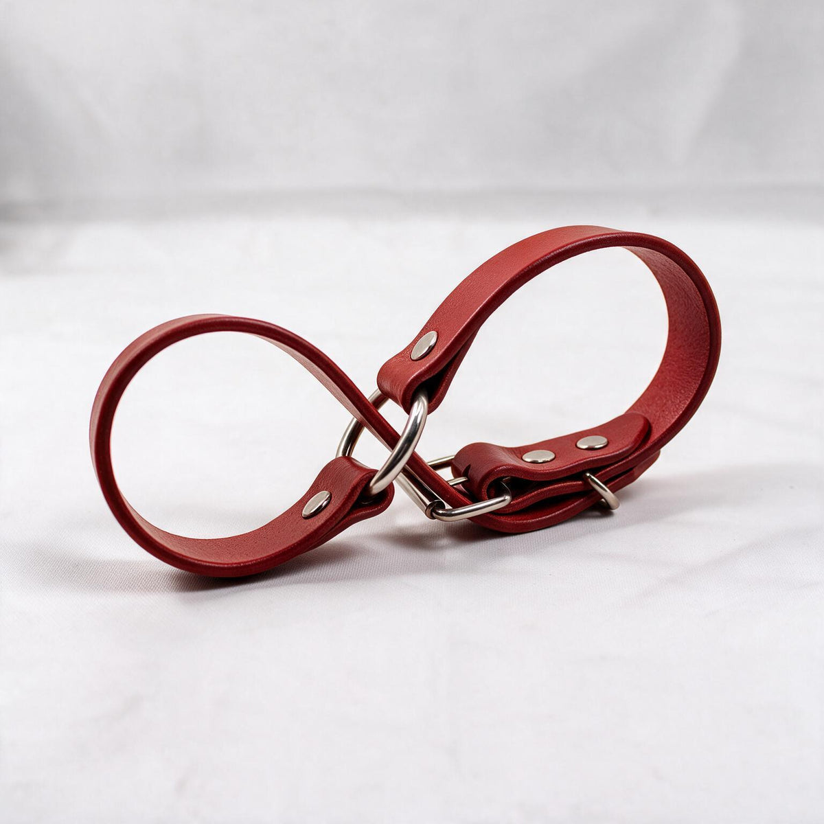 A red leather strap with metal buckles and clips is shown against a white background.