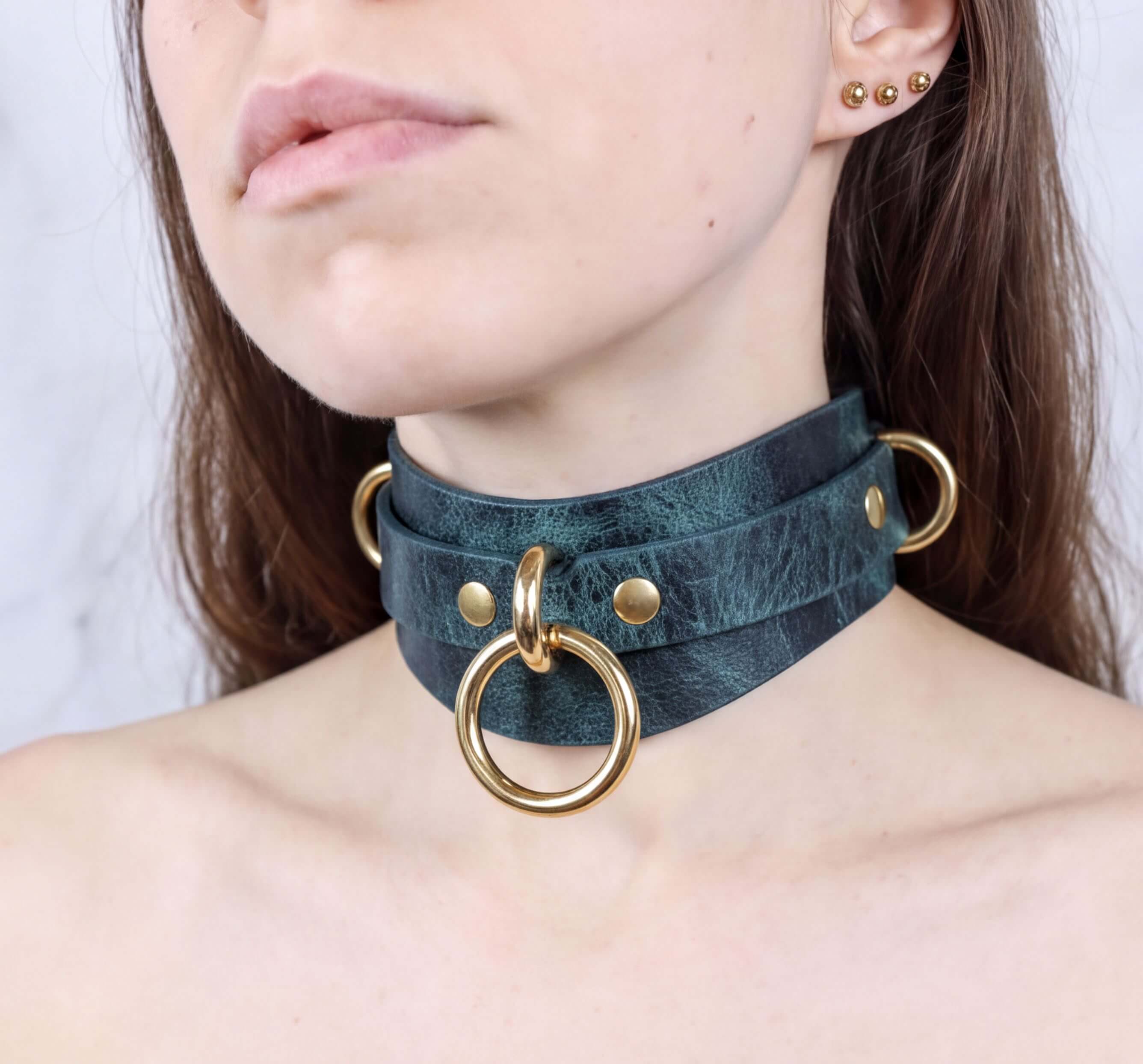 A close-up of a woman's neck and chest area wearing a dark green choker necklace with gold-colored metal rings.
