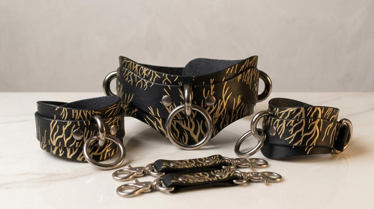 A set of black leather cuffs with gold leaf patterns, featuring multiple rings and buckles, arranged on a white surface.
