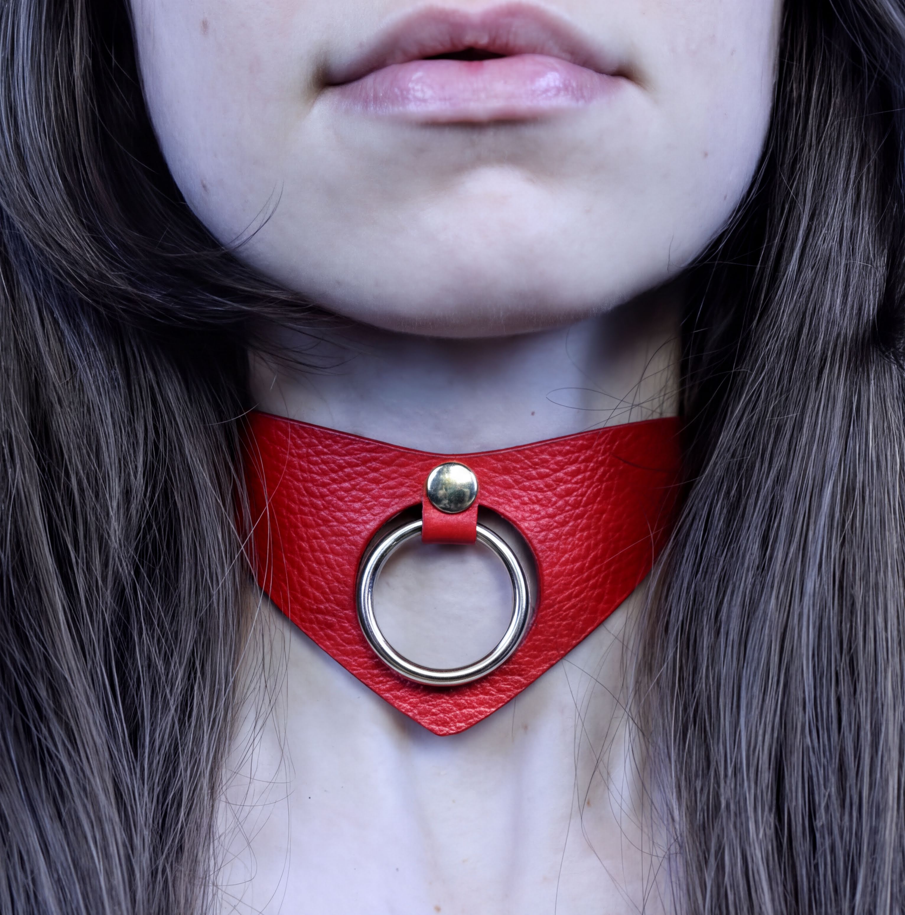 A close-up of a person's neck and chest area, featuring a red leather choker necklace with a metal ring.