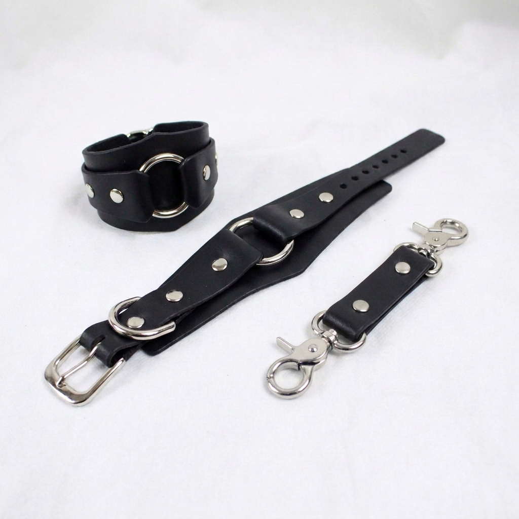 A black leather strap with metal studs and a metal buckle, along with a metal clasp and a metal hook, are displayed on a white surface.