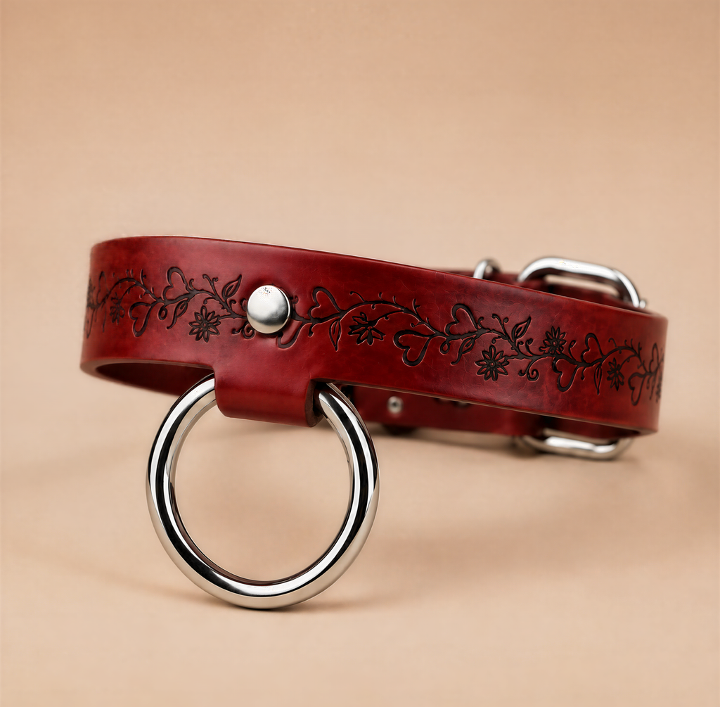 A red leather dog collar with a metal ring and a floral design on the band.