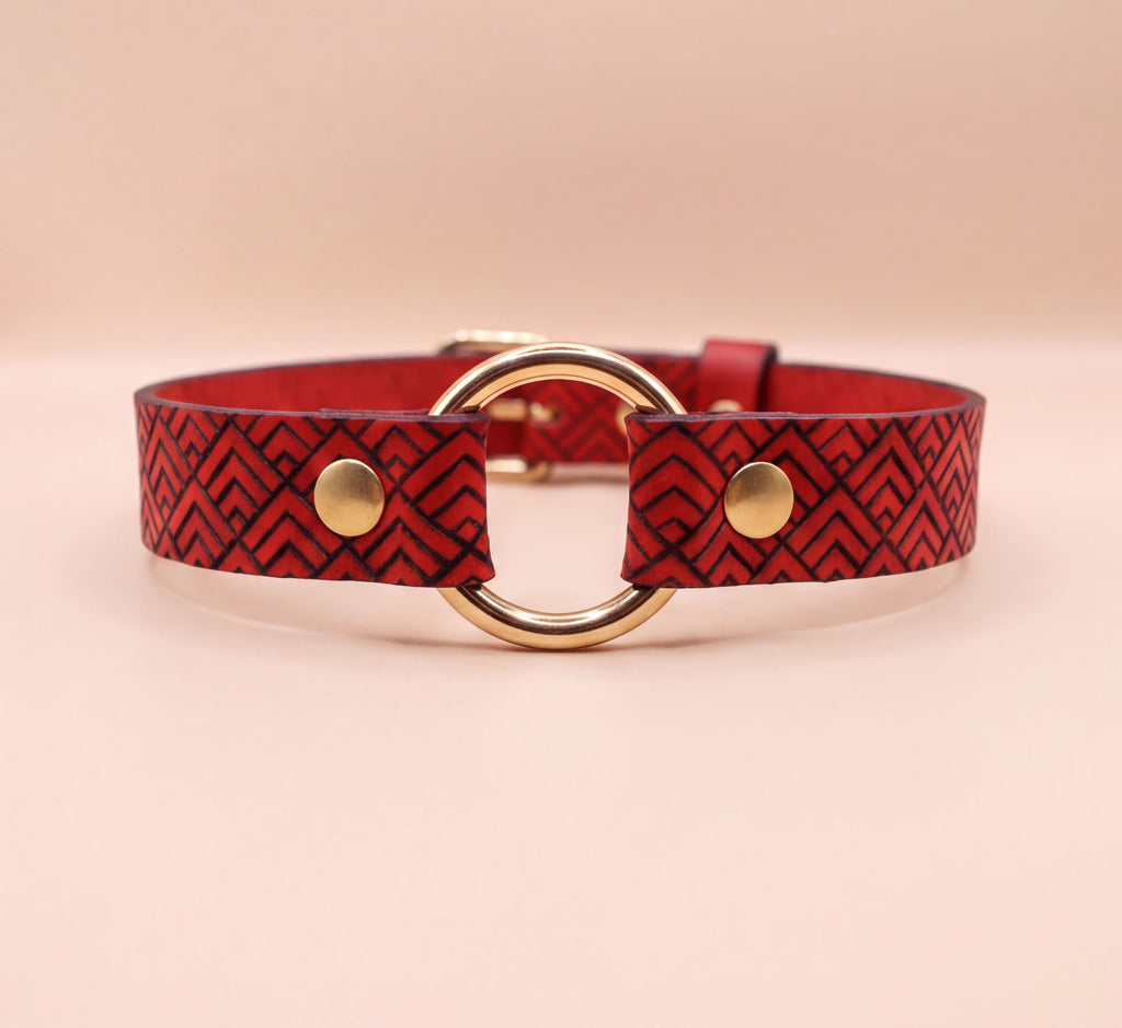 A red leather collar with a gold-colored buckle and two circular buttons.