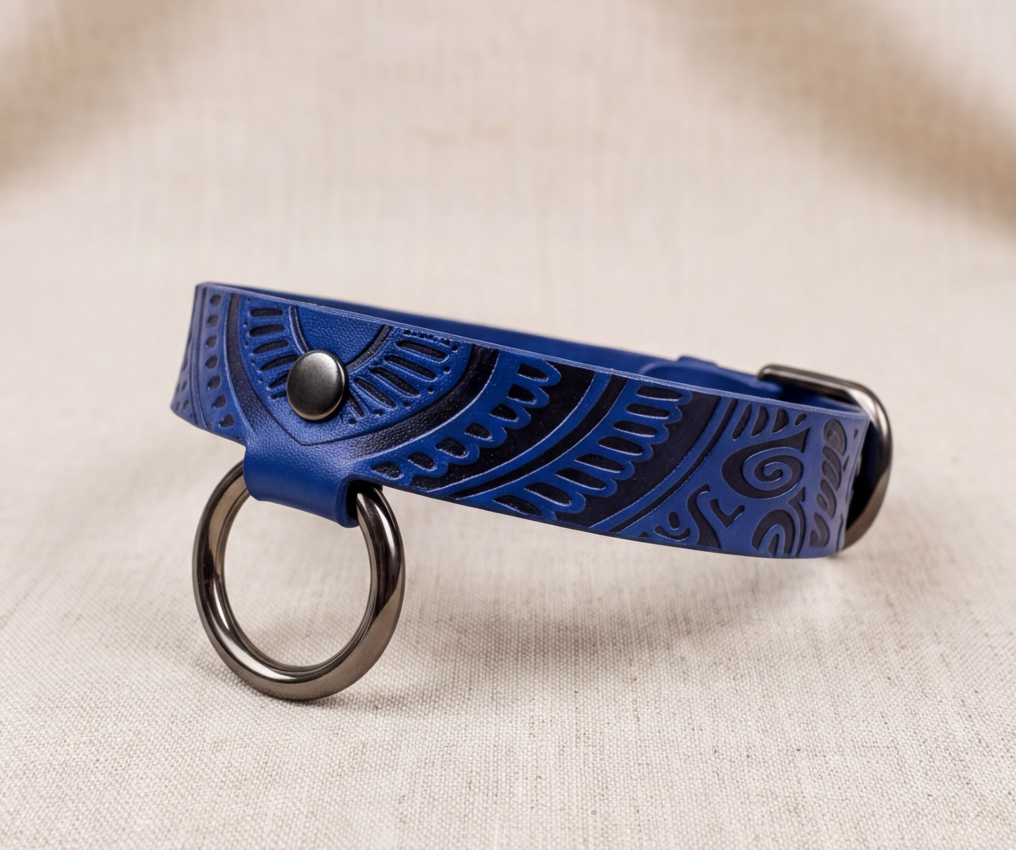 A blue leather collar with a metal ring and a decorative pattern on the surface.