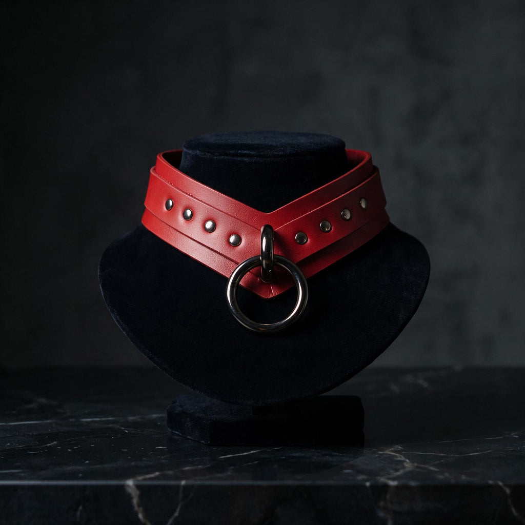 A red leather choker necklace with a large circular metal ring is displayed on a black velvet stand against a dark background.