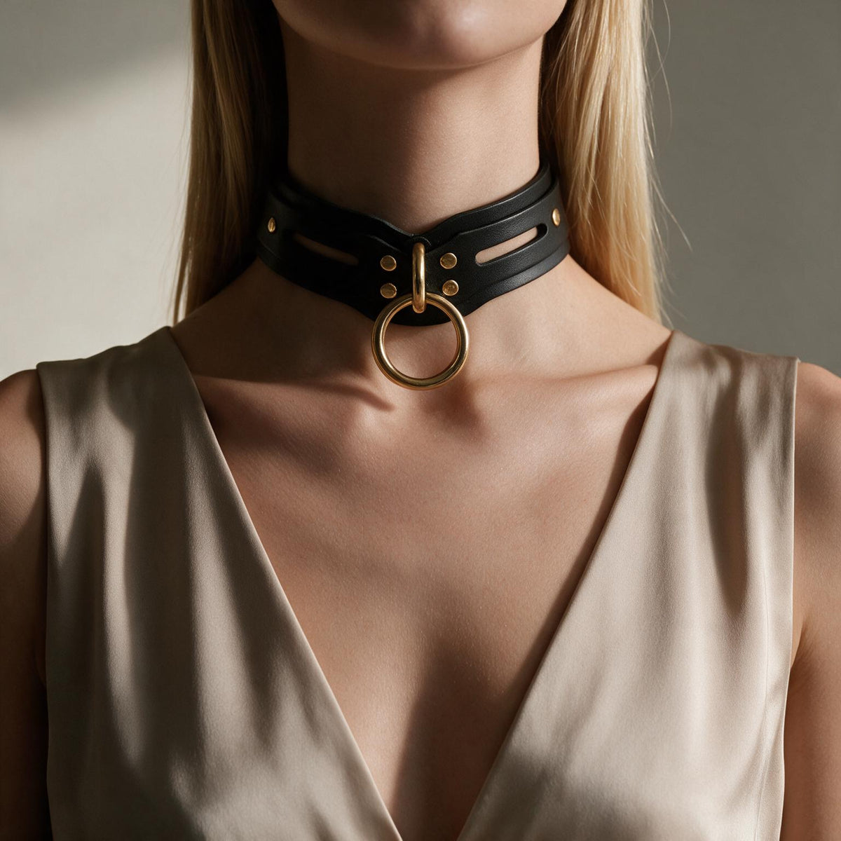 A close-up of a woman wearing a black choker necklace with a gold ring, against a plain background.