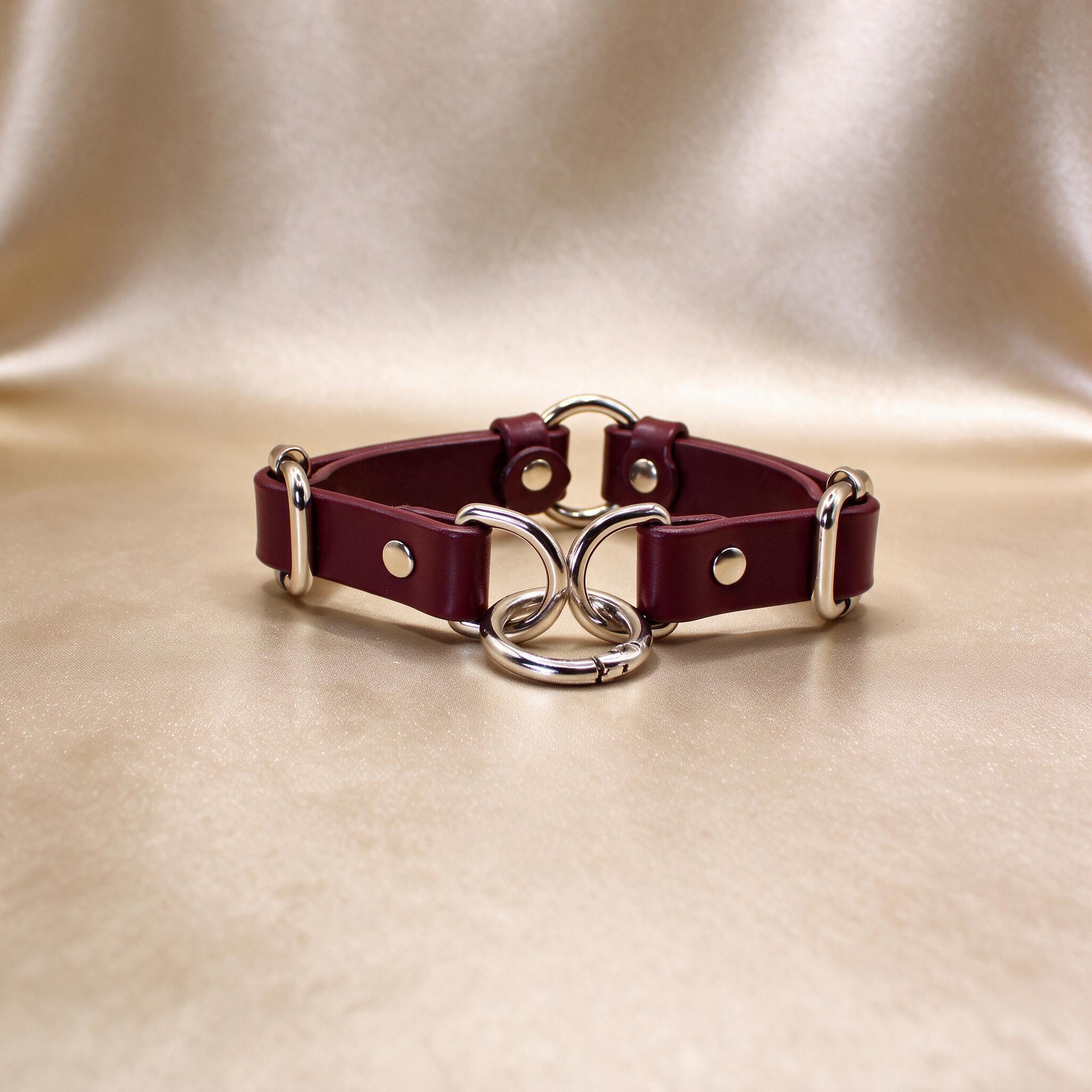 A burgundy leather choker necklace with metal rings and a clasp, displayed on a beige background.