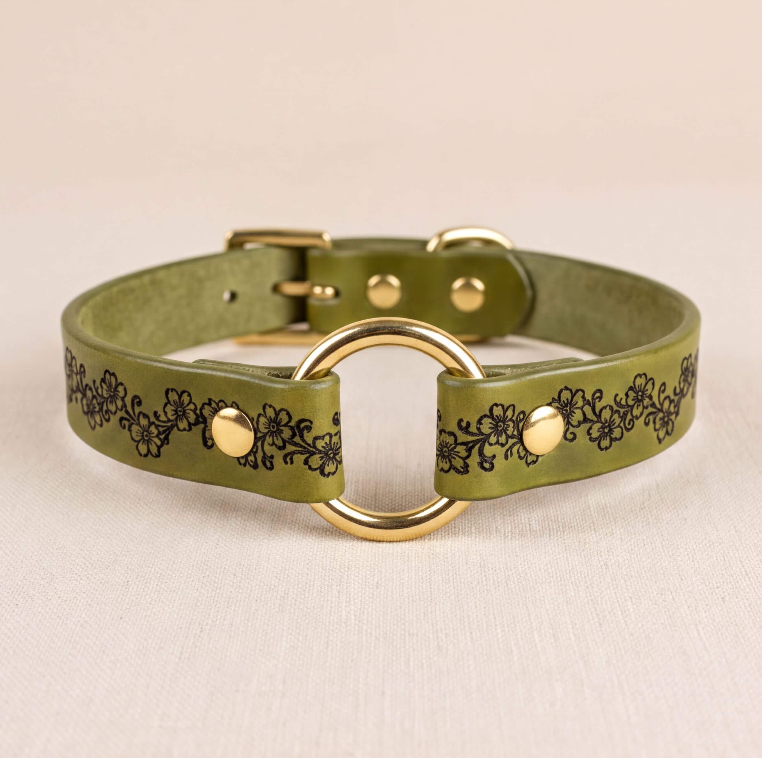 A green leather collar with a gold ring and floral design.