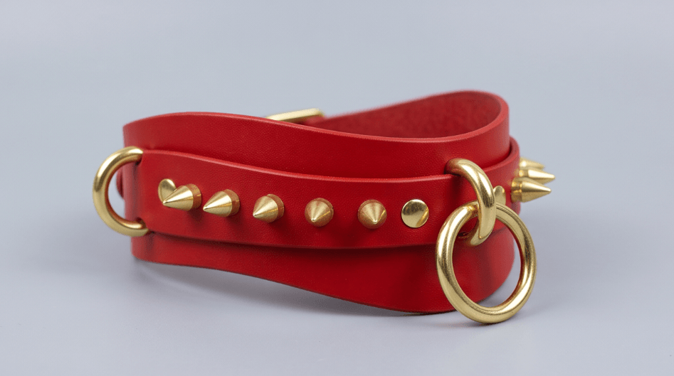 A red leather choker necklace with gold studs and a ring on the front.