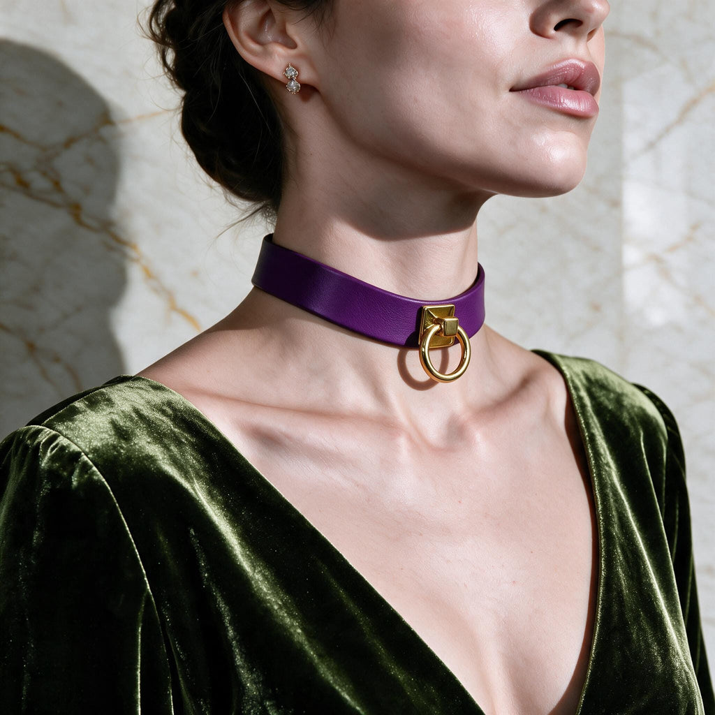 A woman wearing a purple choker necklace with a gold ring on it, and a green velvet dress, posing against a marble wall.