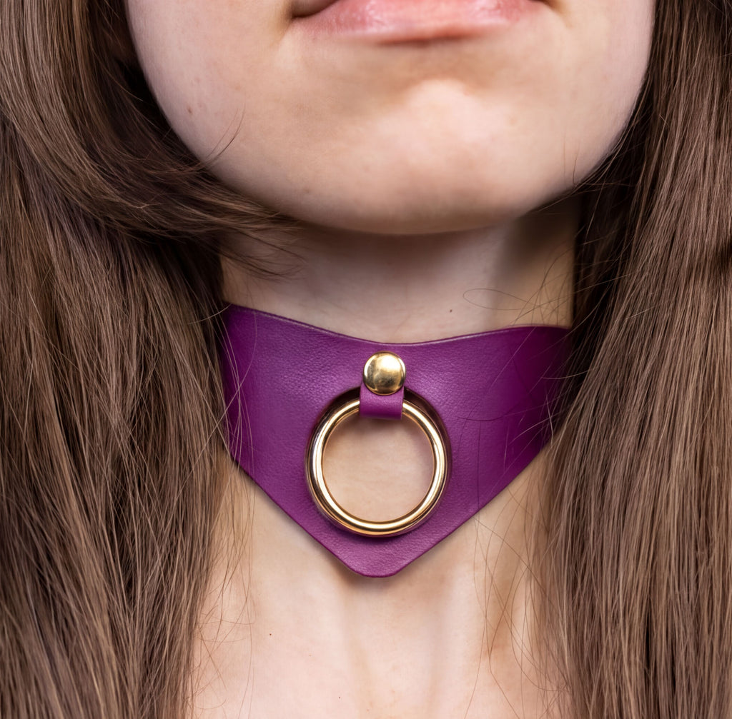 A close-up of a person's neck and chin wearing a purple choker necklace with a gold ring.